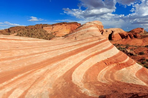 Picture shows an impressive desert landscape with undulating red rocks under a blue sky, Valley of