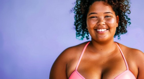 A plus size black afro-american bikini model with curly hair is smiling and wearing a bikini top.