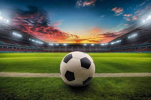 A soccer ball on a green field in soccer football stadium in evening on sunset with floodlights
