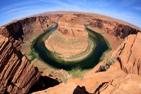 A panoramic view of Horseshoe Bend with steep canyon walls and a river with green water colour,