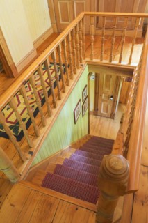 Looking down staircase with maple wood railings and pine wood steps covered with multi-coloured