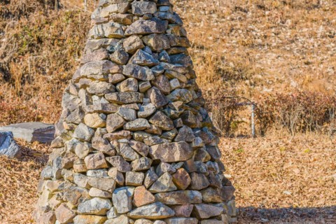 Closeup of pile of stones in the shape of an upside down cone in a public road side park near