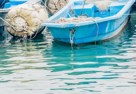 Closeup of small blue fishing boat floating in water tied to a large white buoy in South Korea