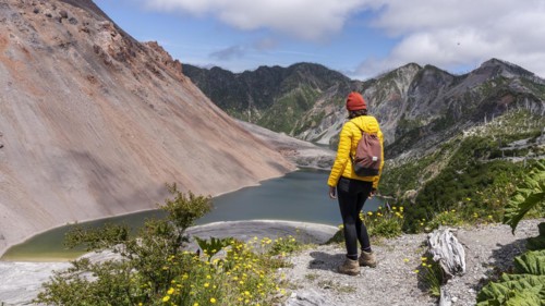 Young woman in yellow jacket standing in front of a volcano, Chaiten Volcano, Carretara Austral,