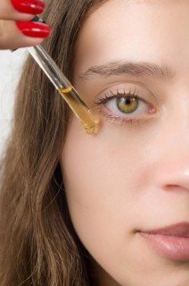Happy young woman applying serum on her face with her eyes open. Beautiful young Brazilian woman
