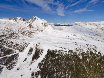Wide-angle aerial view of snow-covered mountains and forest areas under a blue sky, Grau Roig,