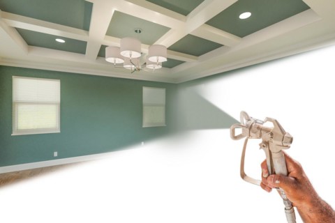 Professional spray painter holding spray gun spraying renovated room over white surface