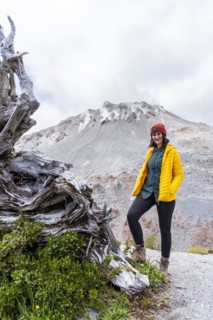 Young woman in yellow jacket standing in front of a volcano, Chaiten Volcano, Carretara Austral,