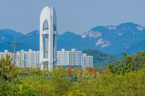 Tall white tower with three sides and cylindrical metal column in middle standing in woodland area