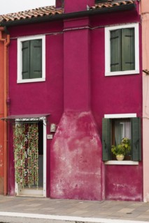 Purple stucco house facade decorated with flowepot in window and curtain over entrance door, Burano