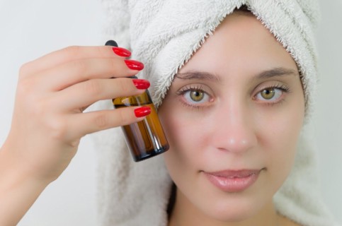 Happy young woman with towel on head holding amber glass bottle of skin serum. Beautiful young