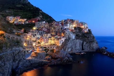 A Mediterranean village on the coast is romantically illuminated by the sea at nightfall, Italy,