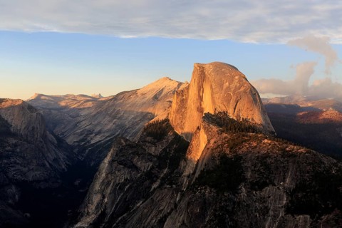 The setting sun bathes Half Dome in orange hues, surrounded by dramatic clouds, Yosemite National