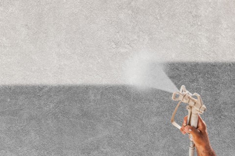 Professional spray painter holding spray gun spraying white paint over grey stucco surface