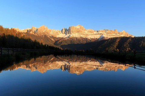 The last rays of the day illuminate the mountains reflected in a calm lake, Trentino-Alto Adige,