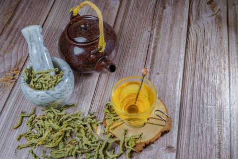 Lemon verbena infusion in a glass cup with a marble mortar and pestle and a ceramic teapot with