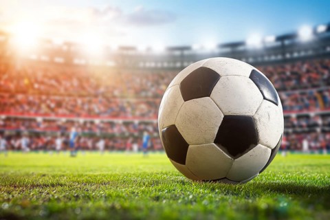 A soccer ball on a green field in soccer football stadium in evening on sunset with floodlights