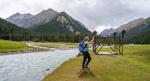 Hiker with backpack standing in front of a drawbridge in a mountainous landscape by the river,