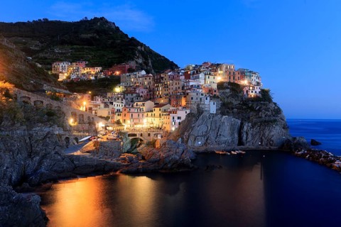Nocturnal atmosphere over a quiet coastal town with shining windows and calm sea, Italy, Liguria,
