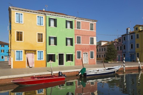 Moored boats on canal lined with orange, green and pink stucco houses decorated with striped