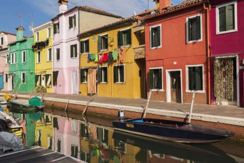 Moored boats on canal lined with pink, red, orange, yellow and green stucco houses decorated with