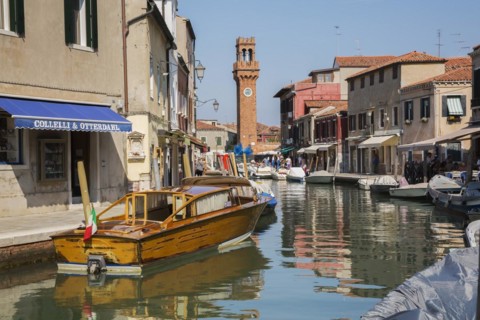 Moored boats on canal with colourful residential buildings, houses, shops, tourists and clock tower