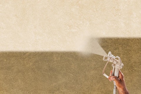 Professional spray painter holding spray gun spraying white paint over brown stucco surface
