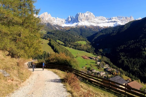 Hikers on a path with a breathtaking mountain panorama and autumnal meadows, Italy, Alto Adige,