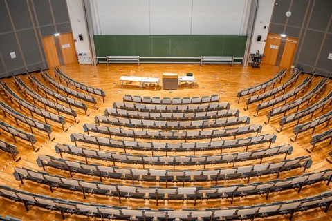 View from above into an empty lecture theatre with rows of seats and lectern, interior photo,