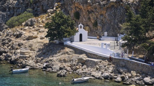 A white church on the Mediterranean Sea on a rocky shore next to parked boats, St Paul's Chapel,