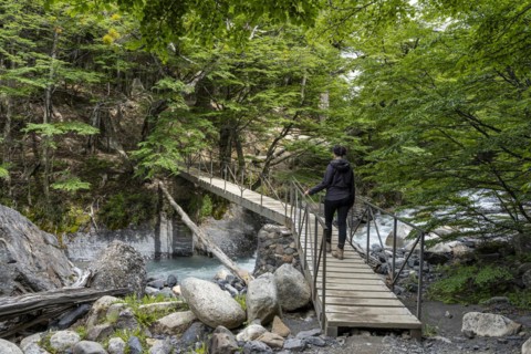 Young woman walking on bridge over meltwater stream, Base of Torres del Paine Hike, Torres de