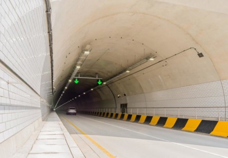 Two lane highway tunnel of white concrete with florescent lights and green arrows on ceiling and