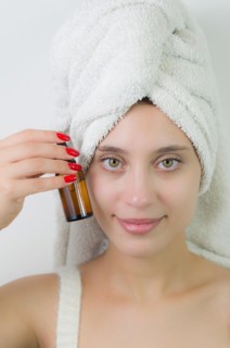 Happy young woman with towel on head holding amber glass bottle of skin serum. Beautiful young