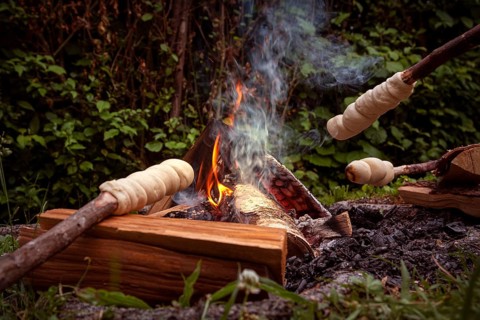 Stick bread is baked over a cosy campfire surrounded by green nature