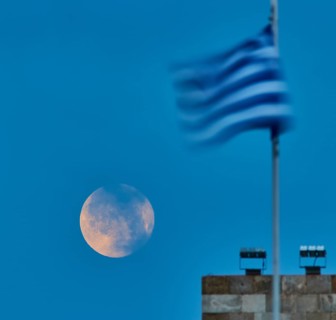 Full moon in semi-darkness next to a blurred flag at dusk, twilight, Mandraki harbour, Rhodes,