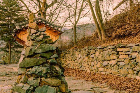 Stone and rock cone shaped tower in front of small wooden oriental building at rural roadside park