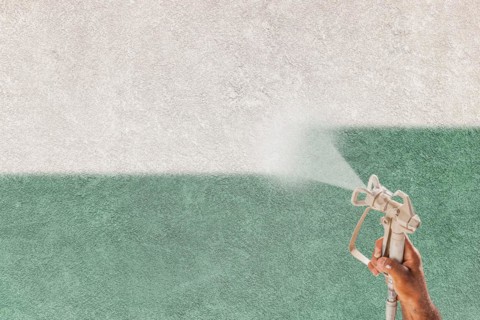 Professional spray painter holding spray gun spraying white paint over teal stucco surface
