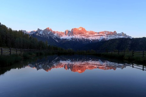 The sunset bathes the mountain peaks in warm light that is reflected in the lake, Trentino-Alto