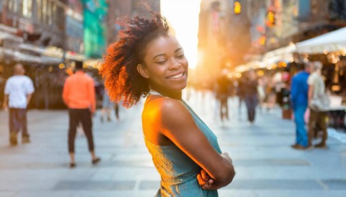 Joyful woman with arms crossed standing on a bustling city street at sunset, AI generated