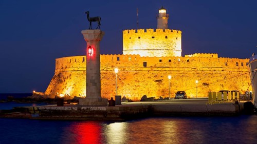 Illuminated historic fortress by the sea at dusk with clear sky and lighthouse, night shot,
