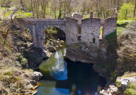 Partially destroyed old stone bridge over a river, surrounded by lush greenery, Bridge of the