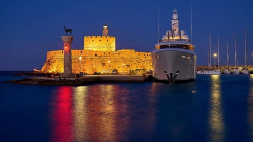 An illuminated castle and a luxury yacht lie by the sea at night with glowing reflections in the