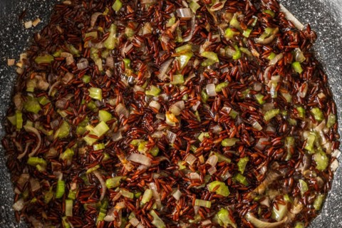 Closeup top view of frying pan with pink rice, onion and celery