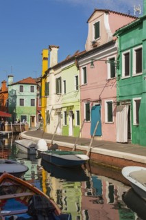 Moored boats on canal lined with pink, yellow and green stucco houses decorated with striped