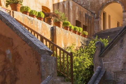 Stone staircase leading to cloister and wall with various plants in terracotta planters in inner