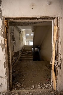 A damaged staircase in a dilapidated building with falling paint and debris at the entrance, ghost