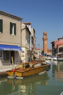 Moored boats on canal with colourful residential buildings, houses, shops, tourists and clock tower