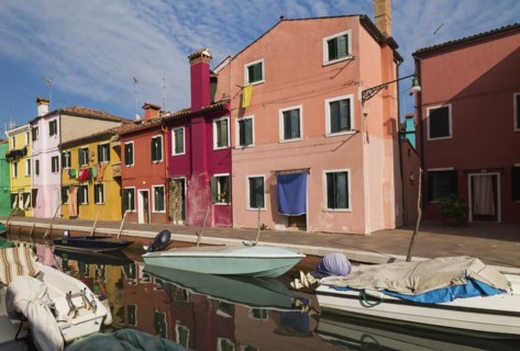Moored boats on canal lined with pink, red, orange, yellow and green stucco houses decorated with