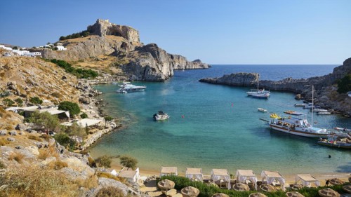 Sunny beach day with a view of a bay, cliffs and parked boats, Paulus Bay, below the Acropolis of