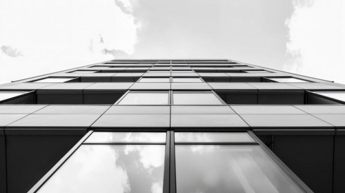 Greyscale image of a skyscraper's glass facade with a cloud reflected in it, AI generated
